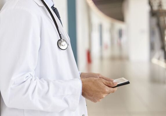 Mid section of doctor using tablet computer in corridor